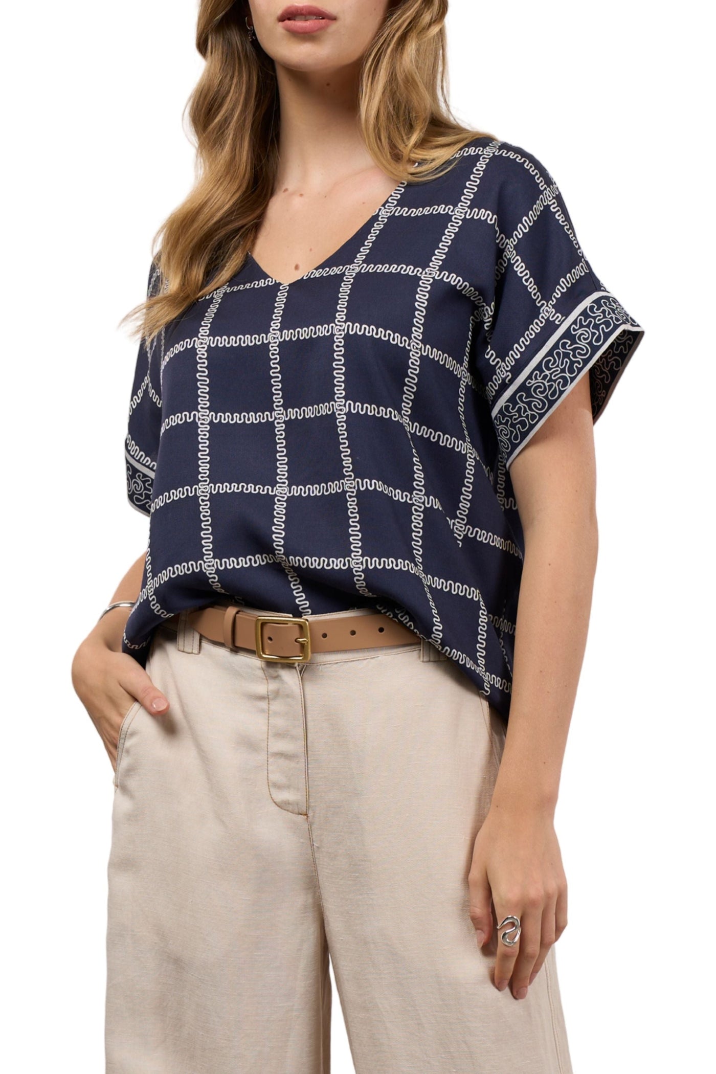 Woman wearing a navy blue and white checkered top with beige pants on a white background