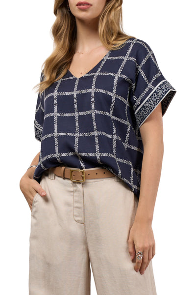 Woman wearing a navy blue and white checkered top with beige pants on a white background