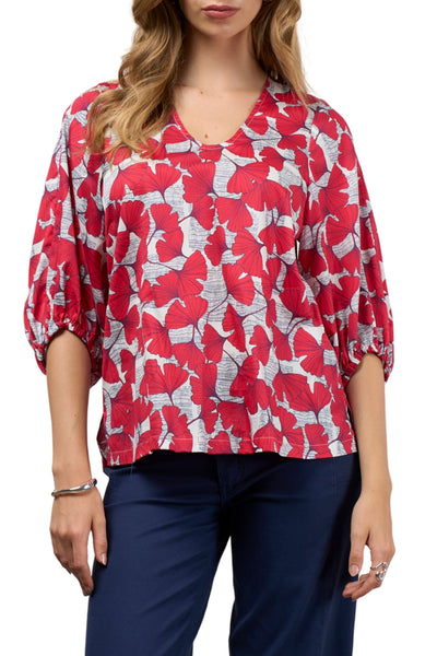Woman wearing a red and white floral blouse with navy pants on a white background