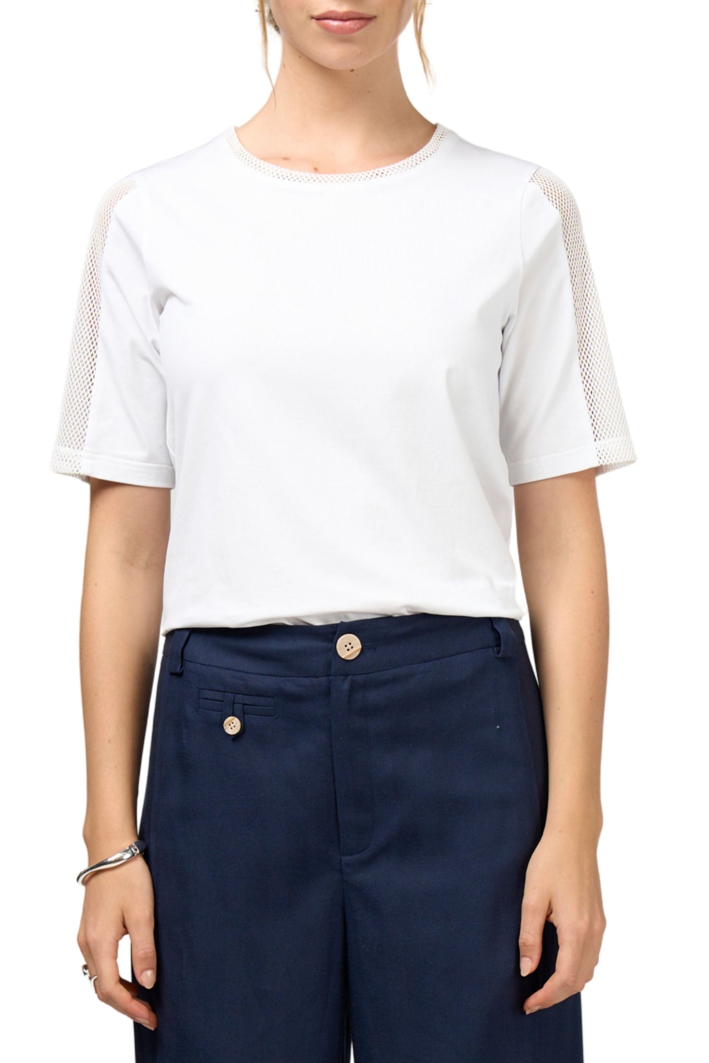 Person wearing a white t-shirt with sheer sleeves and navy pants on a white background