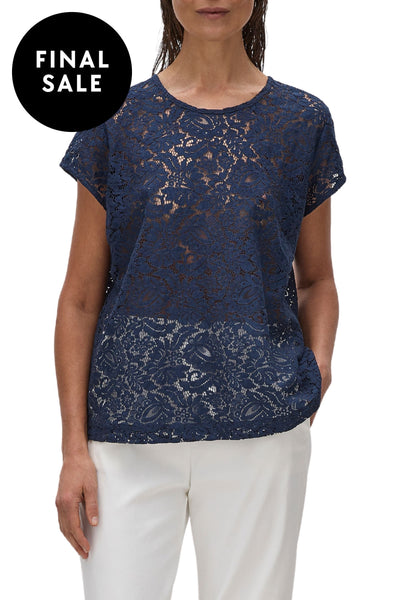 A model wearing a beige, short-sleeved, floral broderie lace top with a scooped neckline.