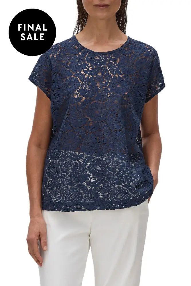 A model wearing a beige, short-sleeved, floral broderie lace top with a scooped neckline.